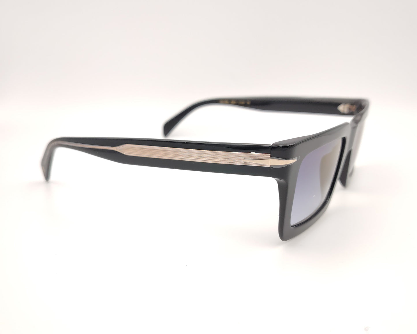 gafas de sol con montura negra cuadrada y gruesa, lentes oscuras y varillas anchas con detalle metálico dorado en relieve