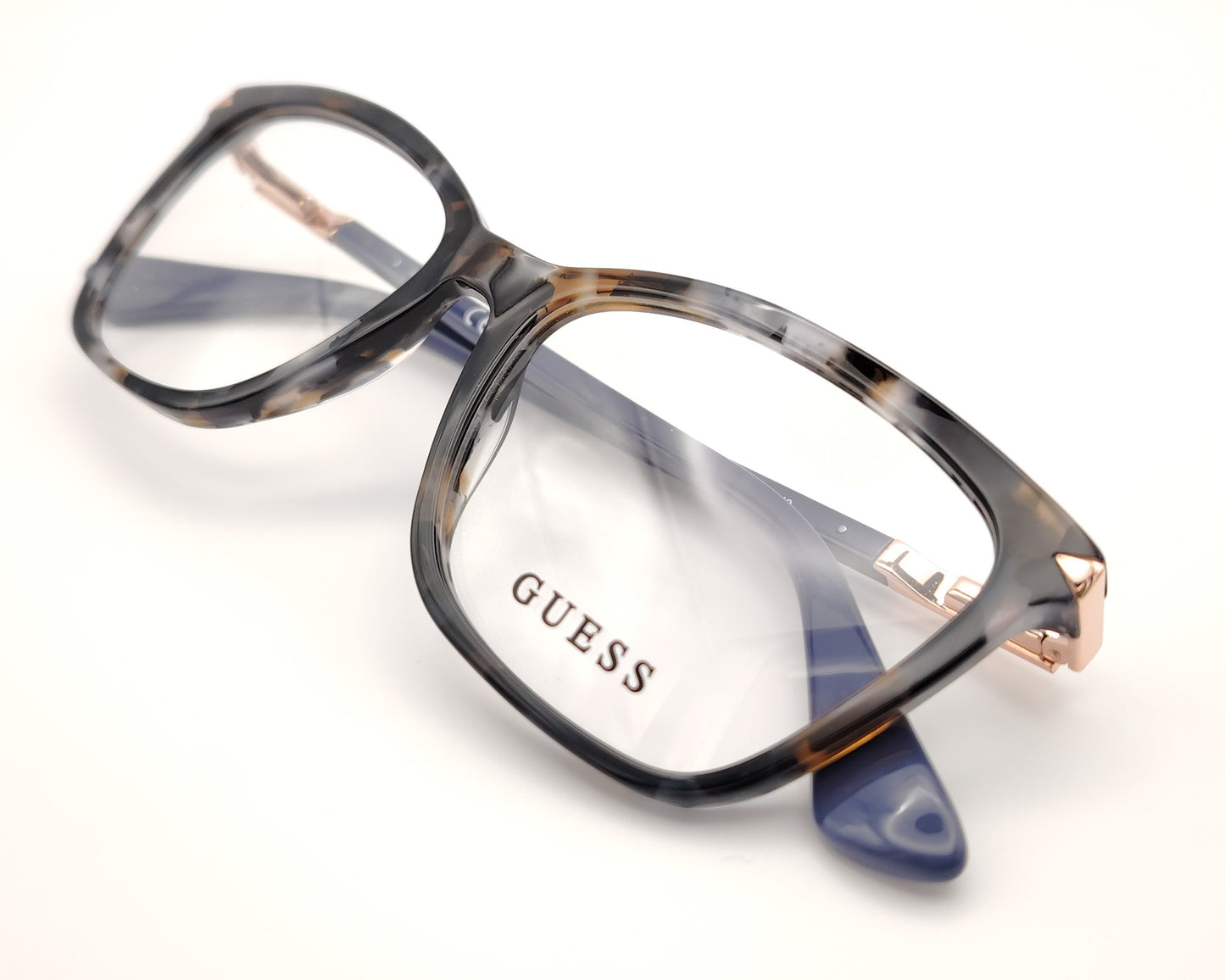 gafas graduadas guess con montura rectangular en carey gris, varillas azul marino y detalles metálicos en dorado rosado