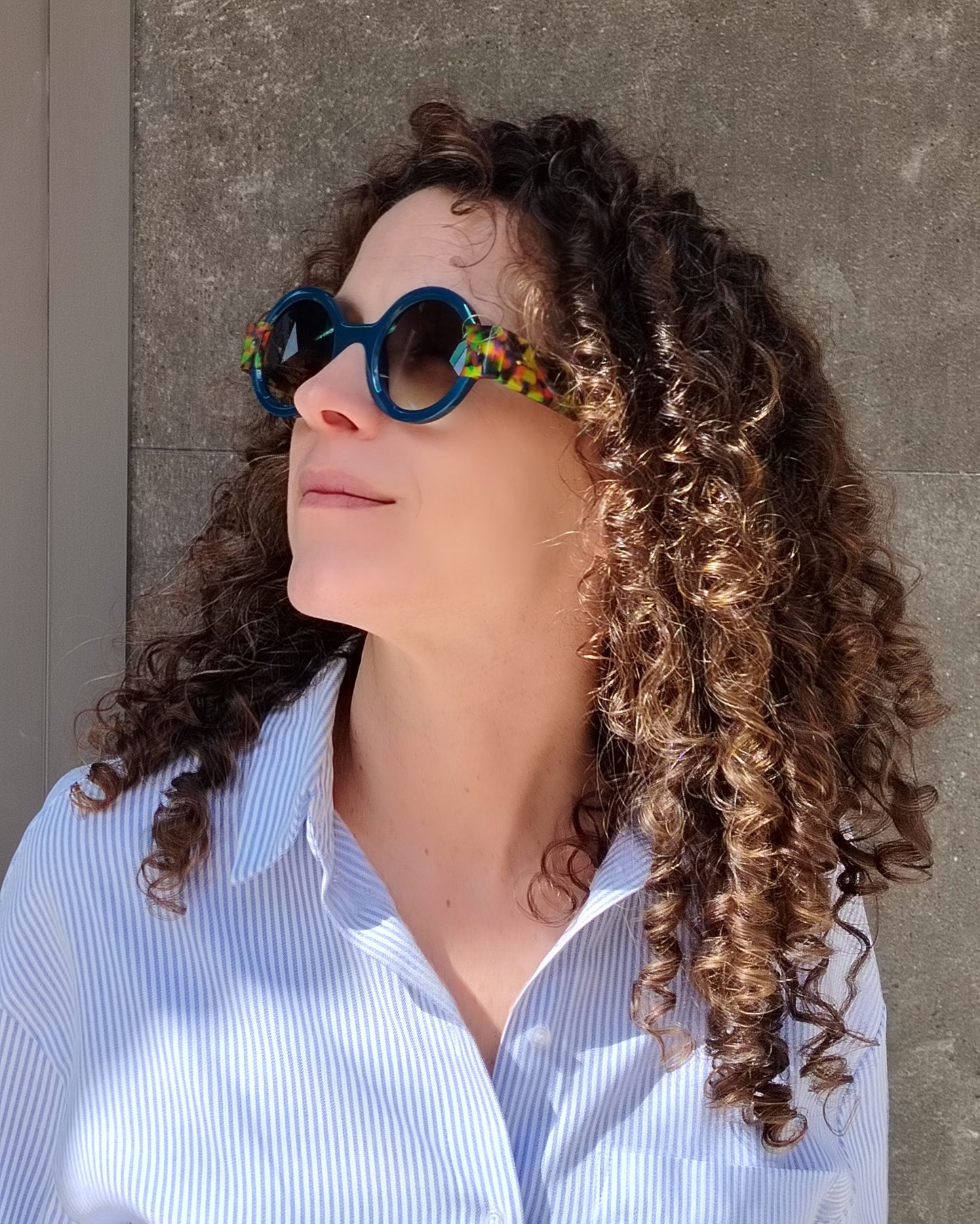 persona con gafas de sol redondas azul oscuro y varillas multicolor tipo confetti