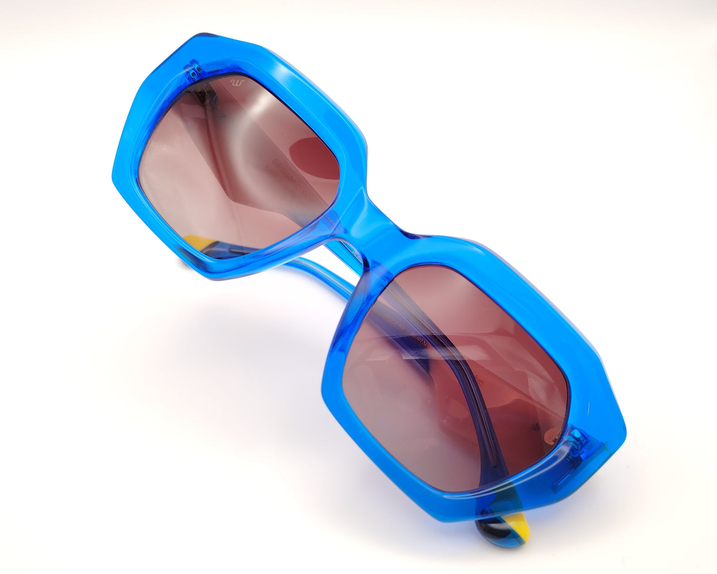 gafas de sol woodys meritxell 04 con montura oversize de acetato azul translúcido diseño geométrico con detalles en rosa y amarillo lentes degradadas en tono marrón varillas con contraste de color