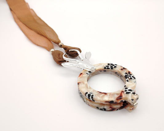 lente plegable de lectura con estampado moteado en tonos tierra y colgante de antílope plateado con cinta  de gasa a juego