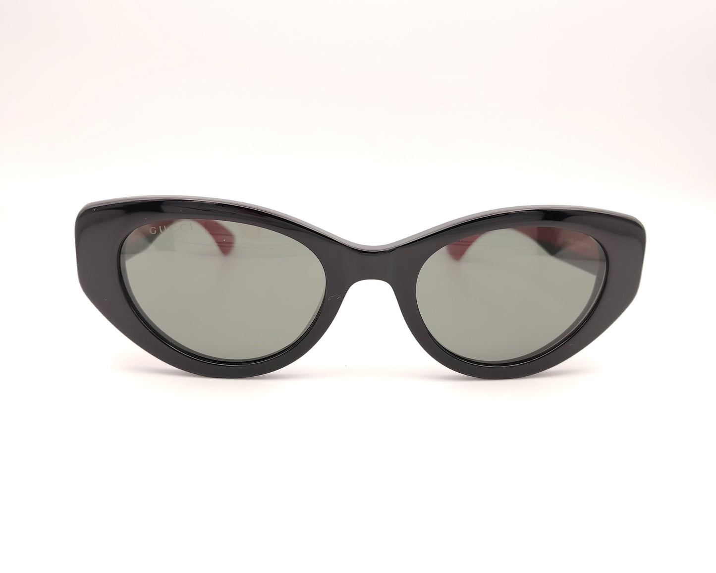 gafas de sol negras estilo cat eye con patillas verdes y rojas y logo dorado


