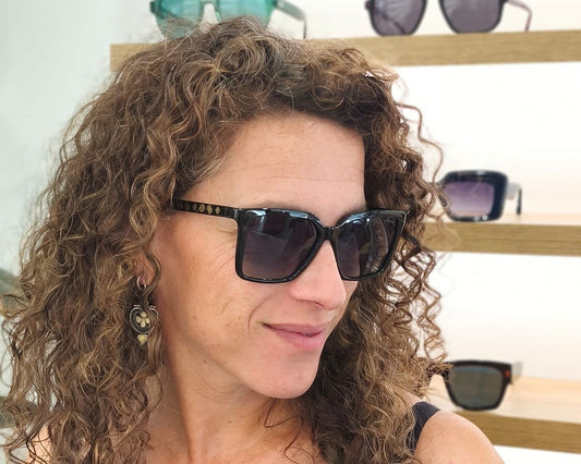 gafas de sol negras con montura en forma cuadrada, cristales degradados en tonos azulados y detalles dorados con símbolos decorativos en la varilla