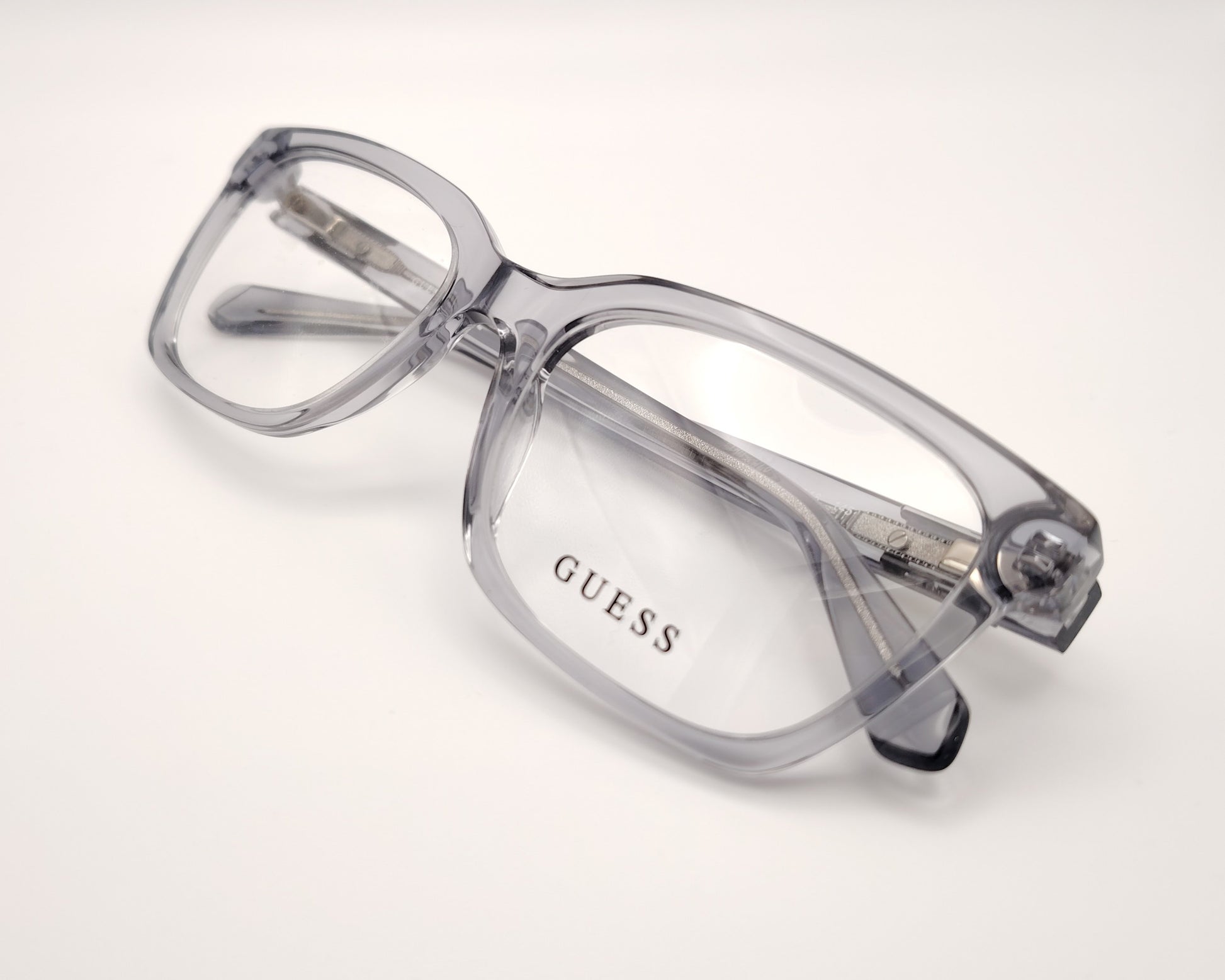 guess gu50132 020 montura elegante en acetato gris transparente con un diseño rectangular, estructura ligera y cómoda perfecta para el día a día detalles metálicos en las varillas que aportan un toque distintivo ideal para un look moderno y versátil