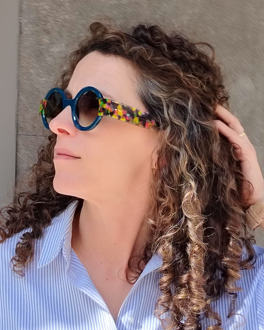 persona con gafas de sol redondas azul oscuro y varillas multicolor tipo confetti
