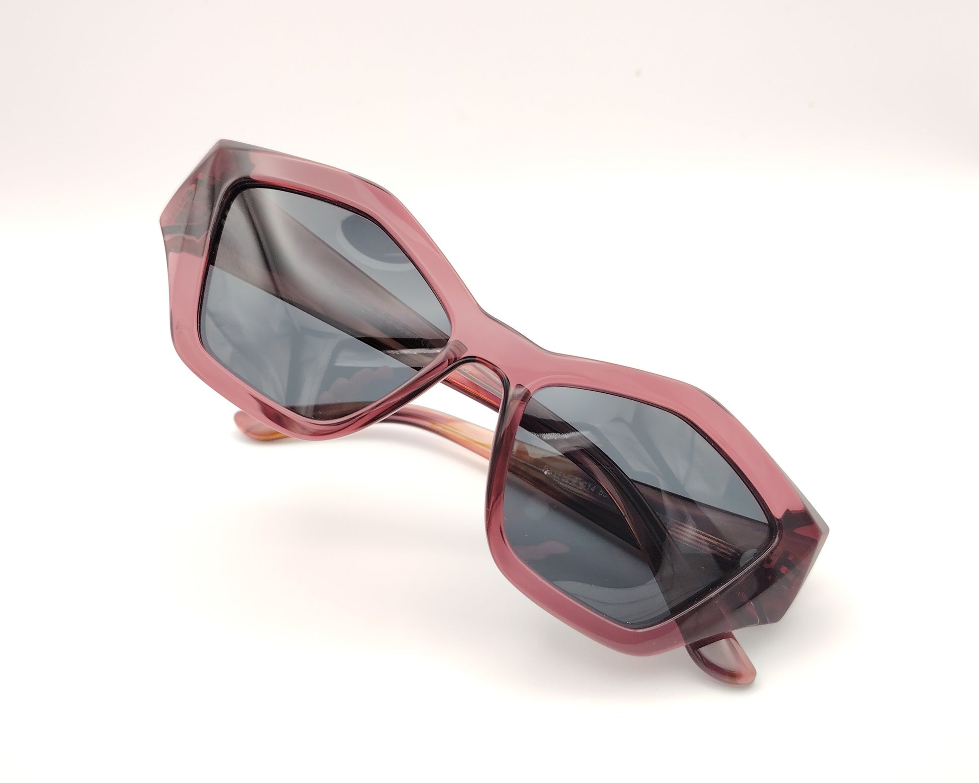 gafas de sol pentagonales con montura rosa translúcida y lentes oscuras polarizadas