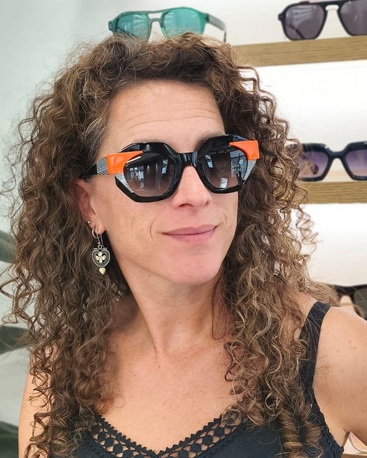 gafas de sol angulosas con montura negra, detalles naranjas y rayas blancas
